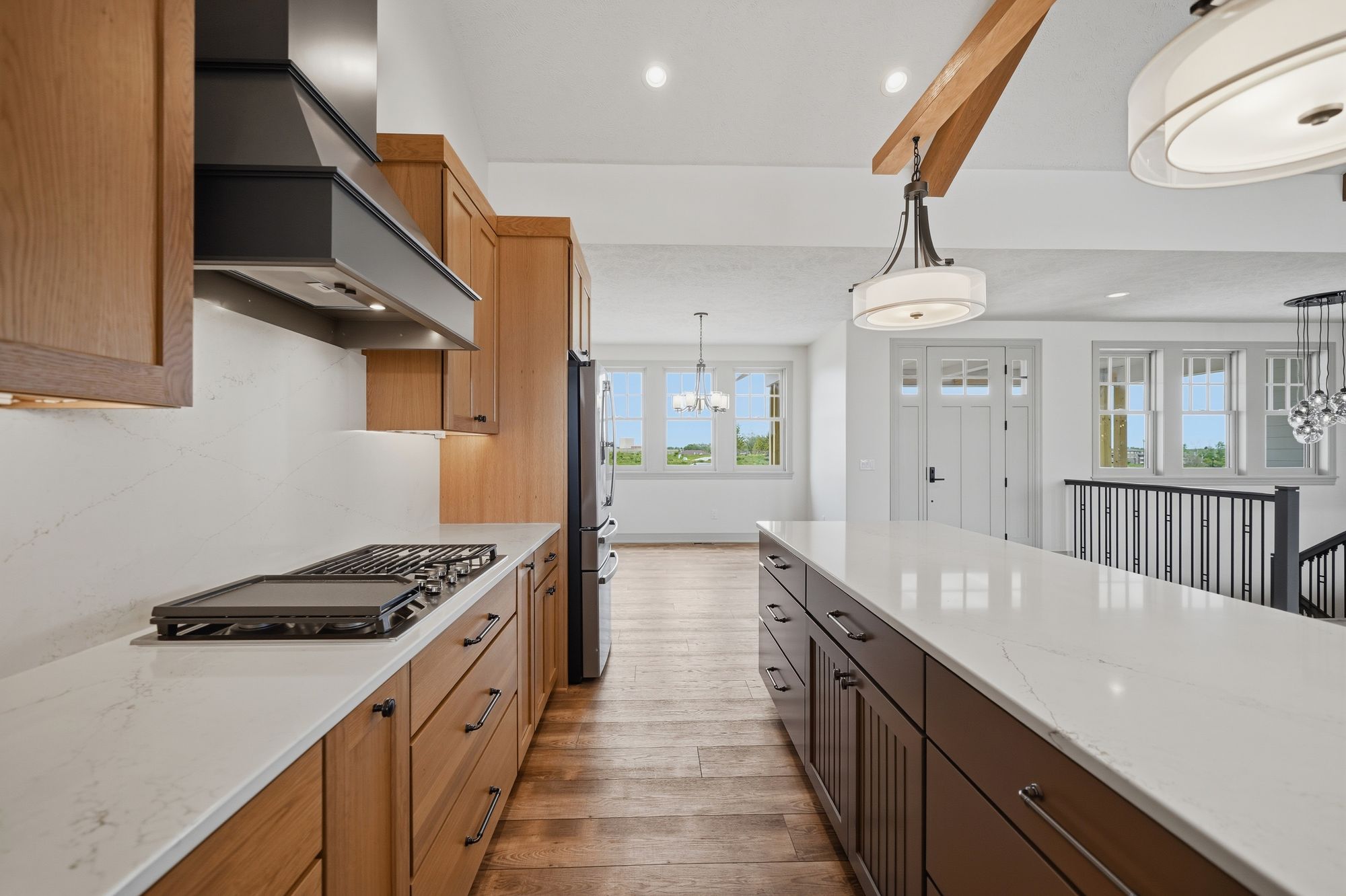 Modern kitchen features light wood cabinetry, white countertops, and a central island with dark wood cabinets. Stainless steel appliances and open floor plan create a bright and airy space.