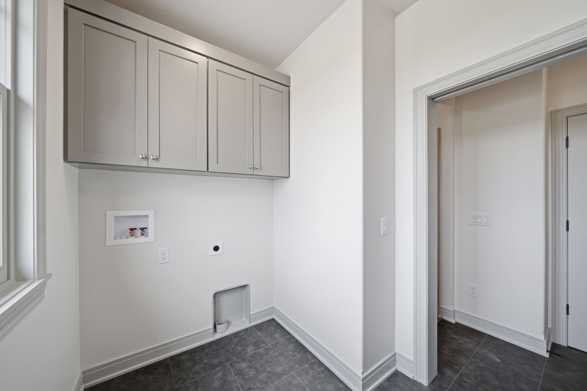 A laundry room features gray cabinets above a hookup area. The room has a gray tile floor and white walls and trim.