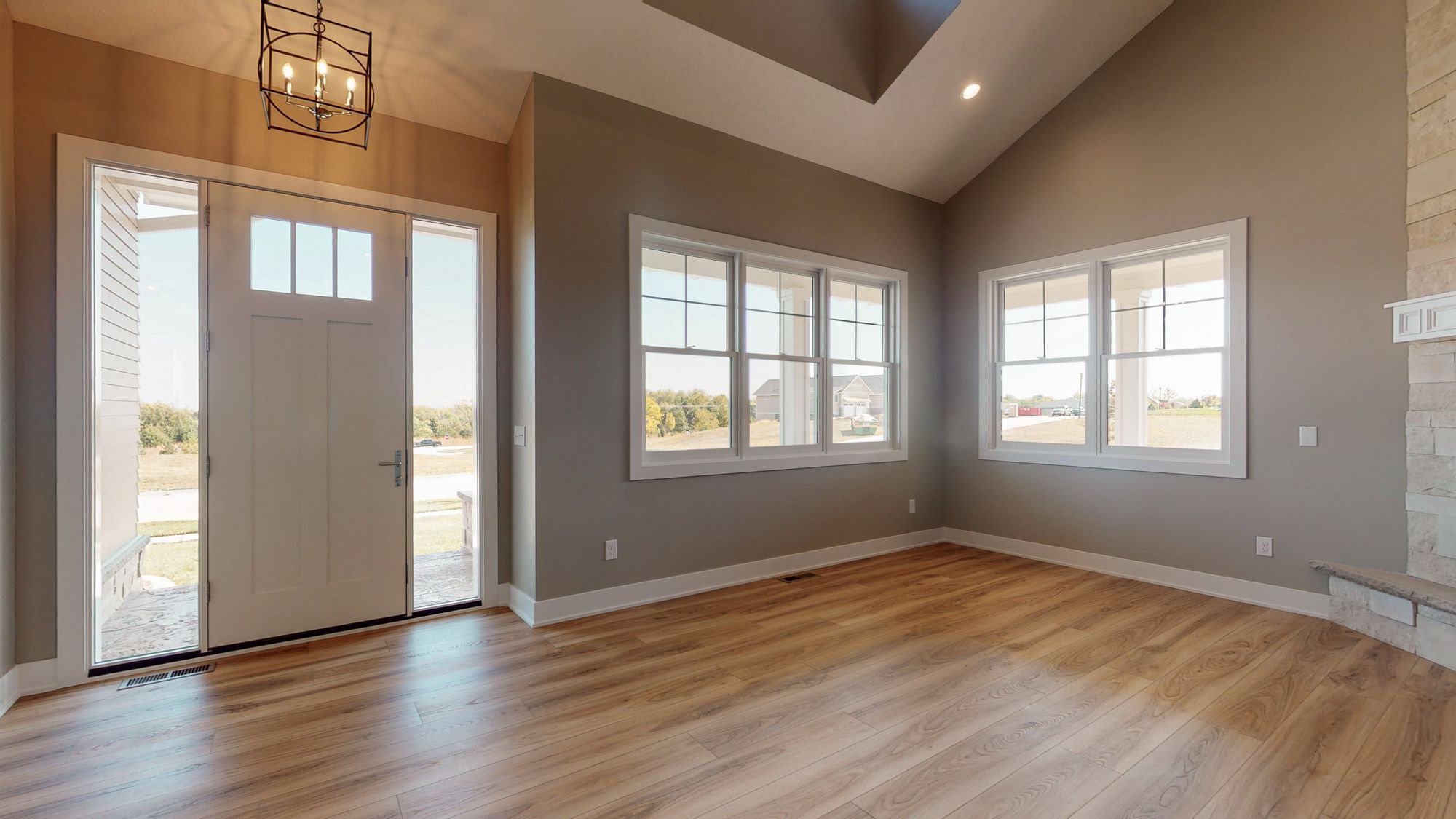 Entryway featuring an open white door, two windows with white frames, light hardwood floors, and a modern chandelier. The walls are painted a neutral tone, and there is a high ceiling.