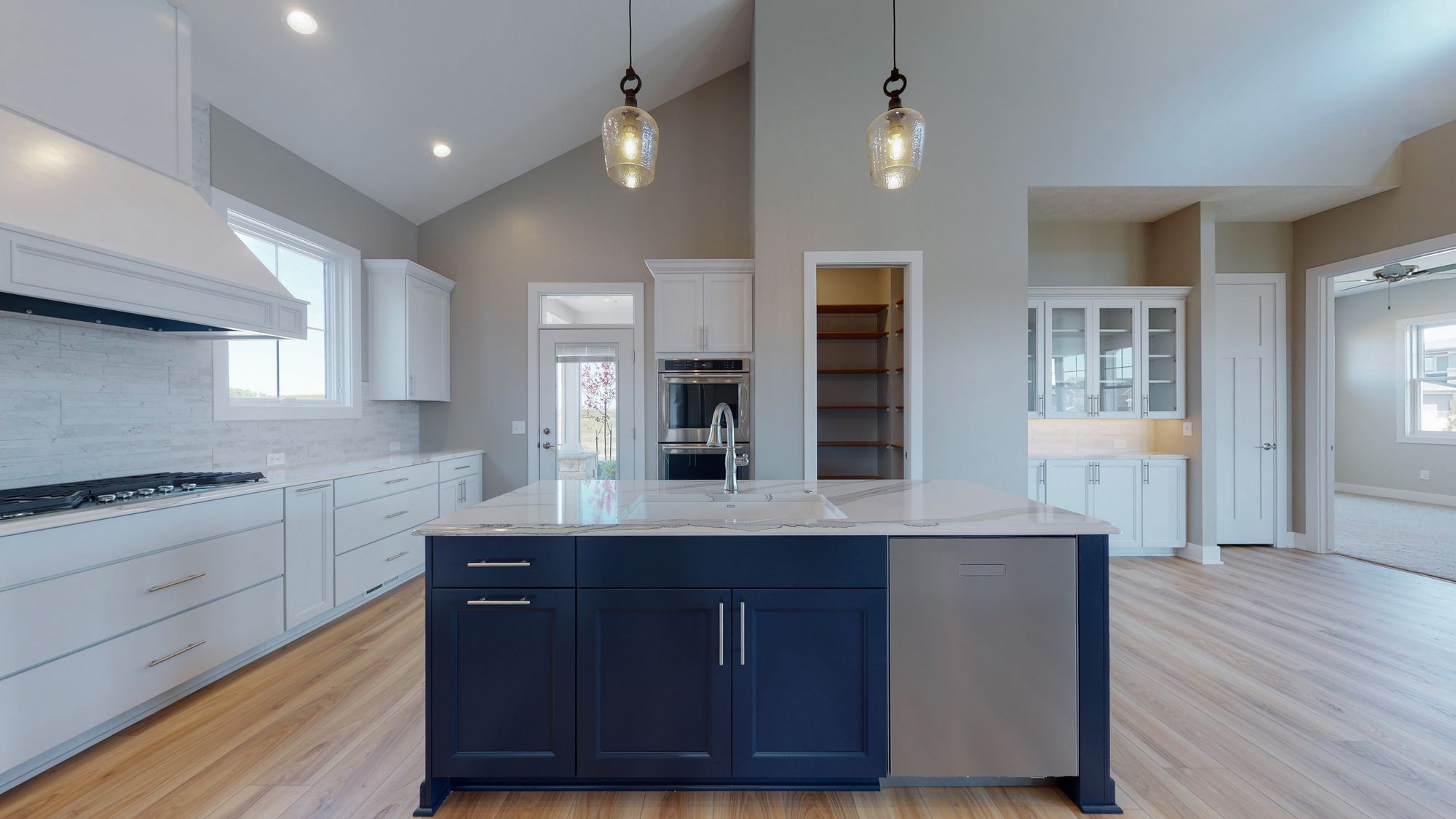 Bright kitchen with navy island, white cabinets, and wood floors. Open concept kitchen featuring stainless steel appliances, marble countertops, and modern pendant lighting.