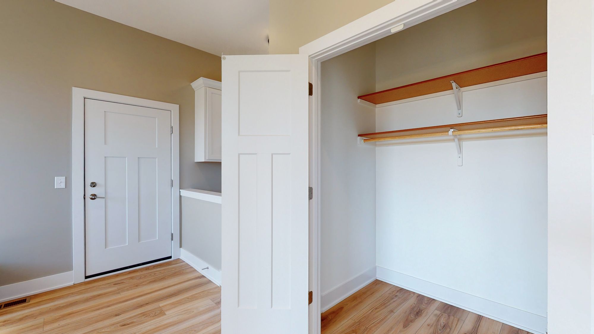 Mudroom featuring an open closet with built-in shelving, a white paneled door, and light wood-look flooring. The walls are painted in a neutral beige and gray combination.
