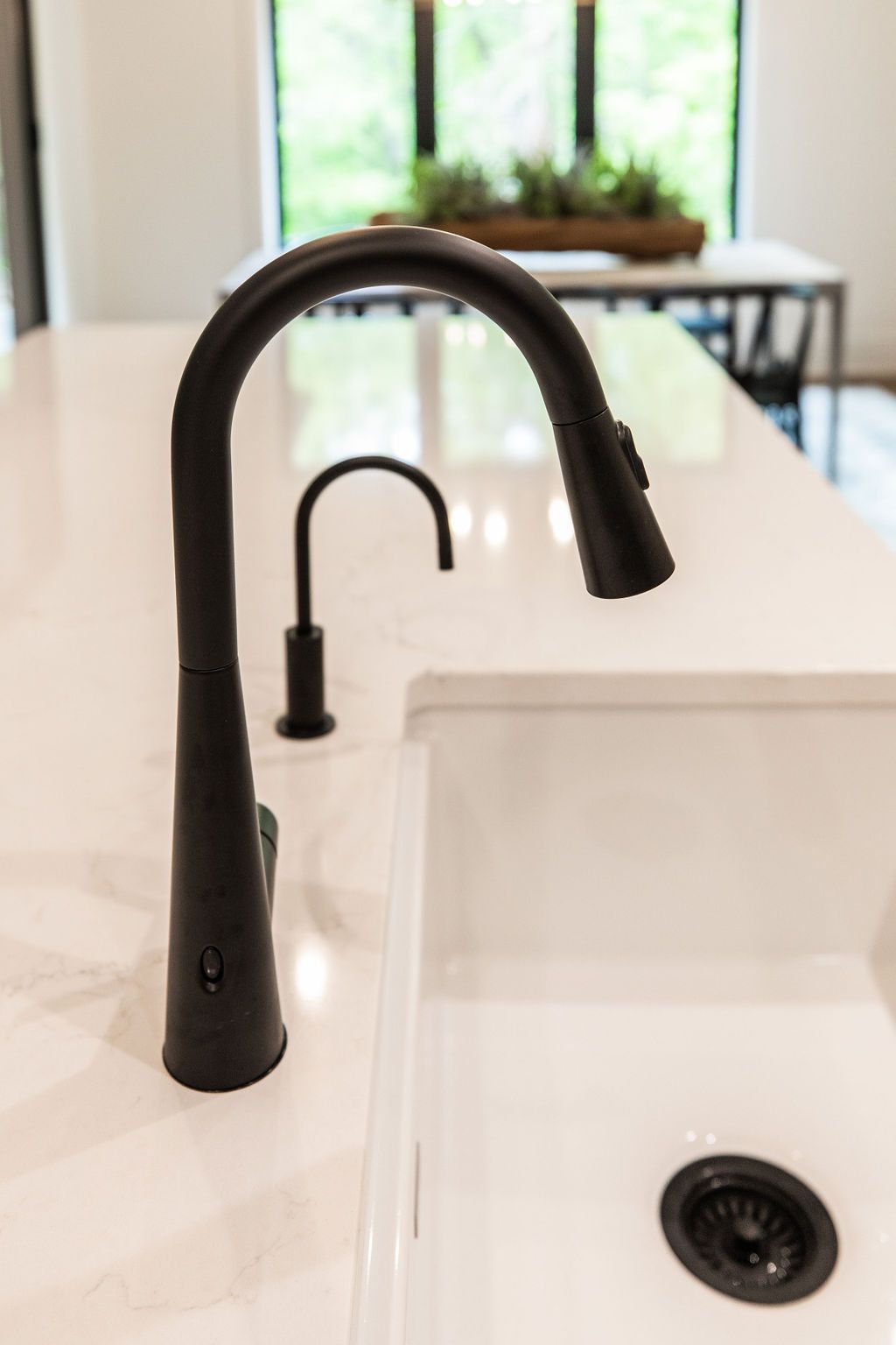 Modern kitchen features a white sink, black faucet, and marble countertops. The sink is located on an island in the center of the kitchen.