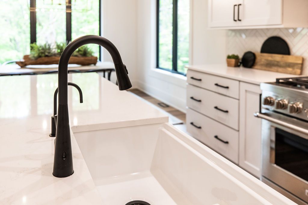 Bright kitchen features a large white farmhouse sink with a matte black faucet. Clean lines and white cabinetry contribute to the modern aesthetic.