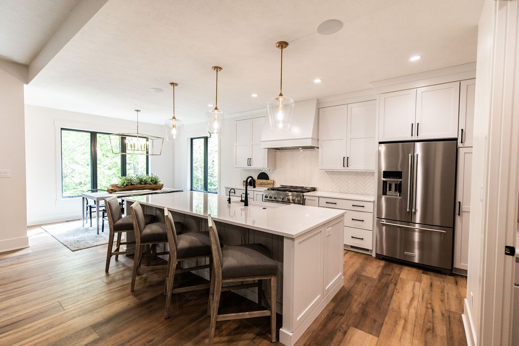 Bright, modern kitchen featuring white cabinetry, a large center island with bar seating, and stainless steel appliances. The space includes hardwood floors and stylish pendant lighting above the island, with a dining area visible in the background.