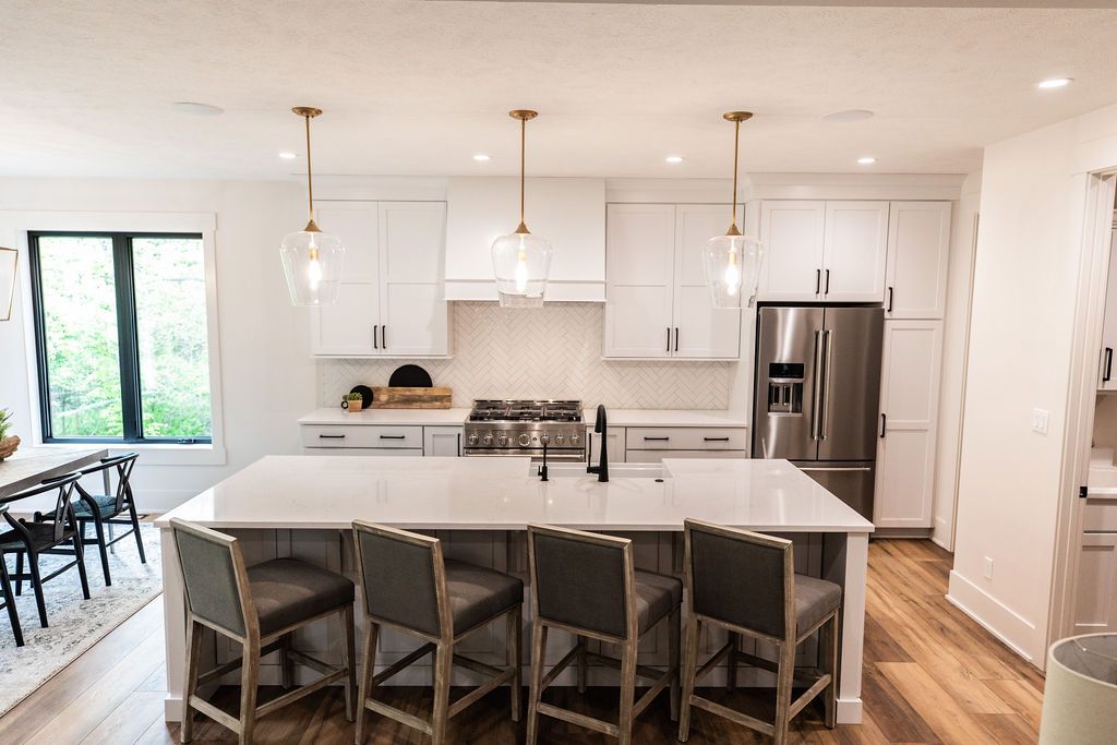 Bright kitchen with a large island featuring seating, light wood flooring, and white cabinetry. Stainless steel appliances complement the modern design.
