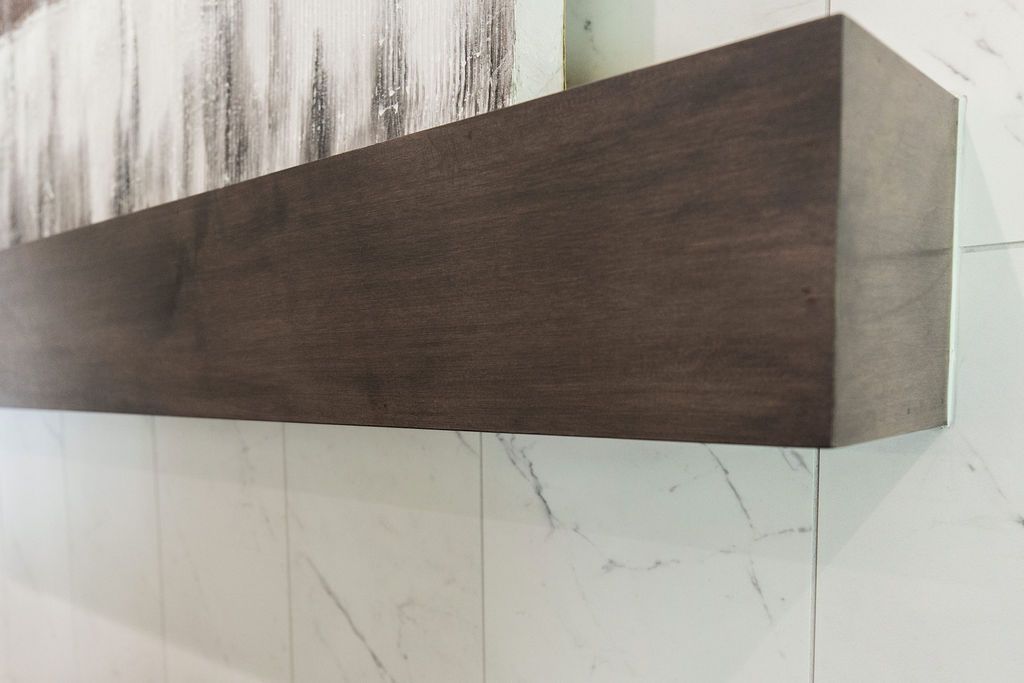 Close-up of a dark stained wood mantel shelf mounted on a white marble tiled wall. Artwork is visible above the mantel.