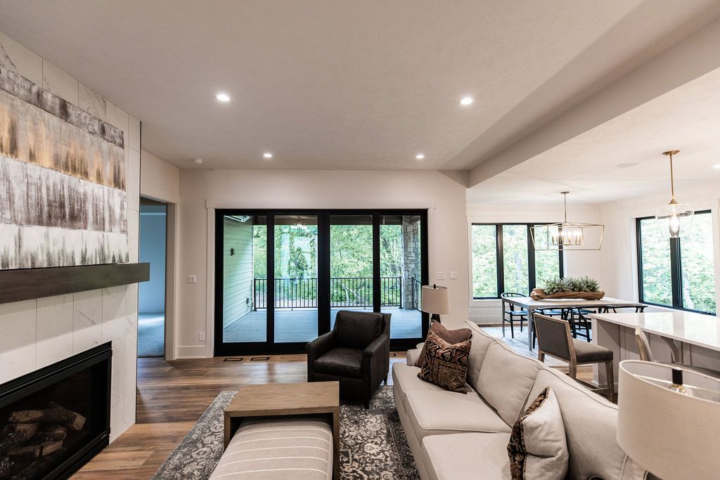Bright living room with hardwood floors, a gray rug, and a light gray sofa. The room features a fireplace with an abstract art piece above, and sliding glass doors that lead to a balcony.