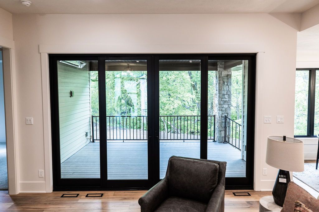 The image shows a bright and airy living room with a large sliding glass door leading to an outdoor deck. The room features hardwood floors and is furnished with a gray armchair.