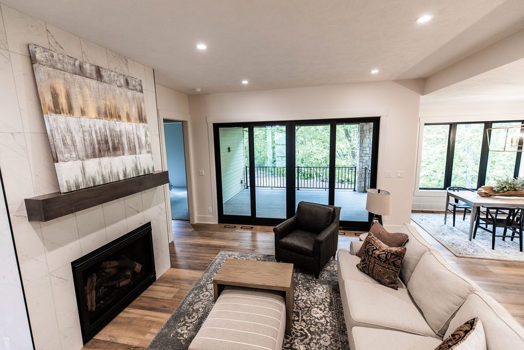 Bright living room with fireplace and sliding glass doors. The room features a white sectional sofa, gray armchair, and wood-look flooring, with a dining area visible in the background.