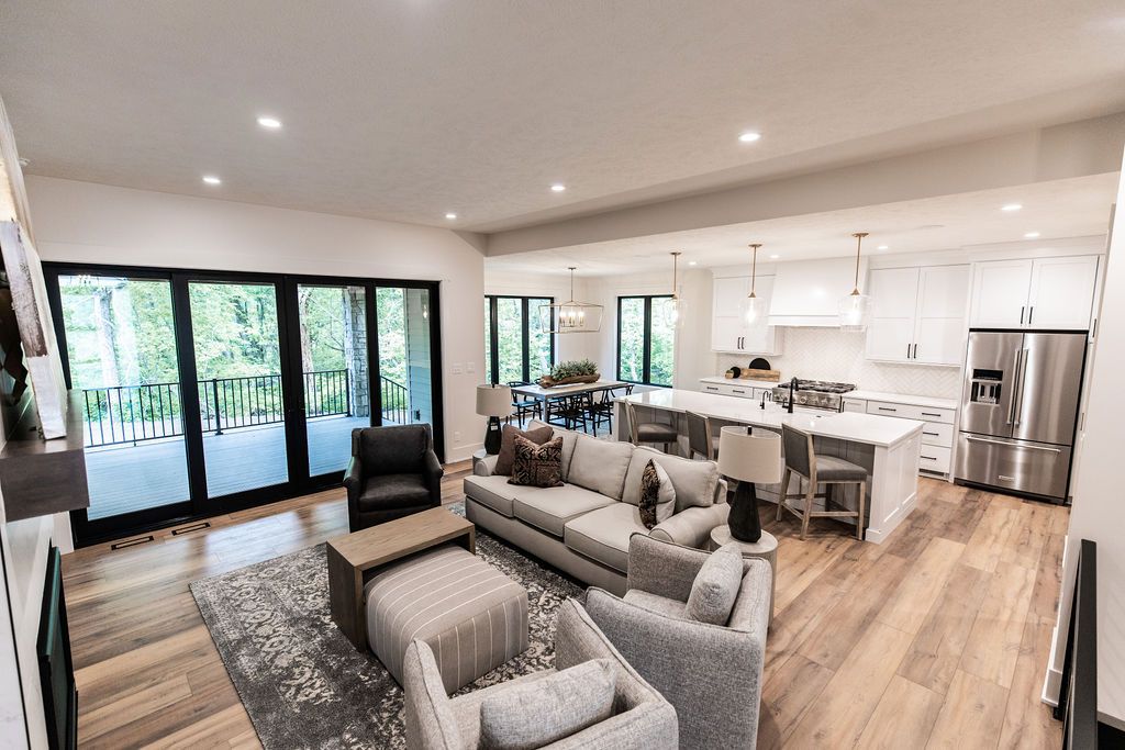 Open concept living room and kitchen features a large sliding glass door leading to a deck. The living room has hardwood floors, a gray area rug, a gray sofa, and two gray armchairs.