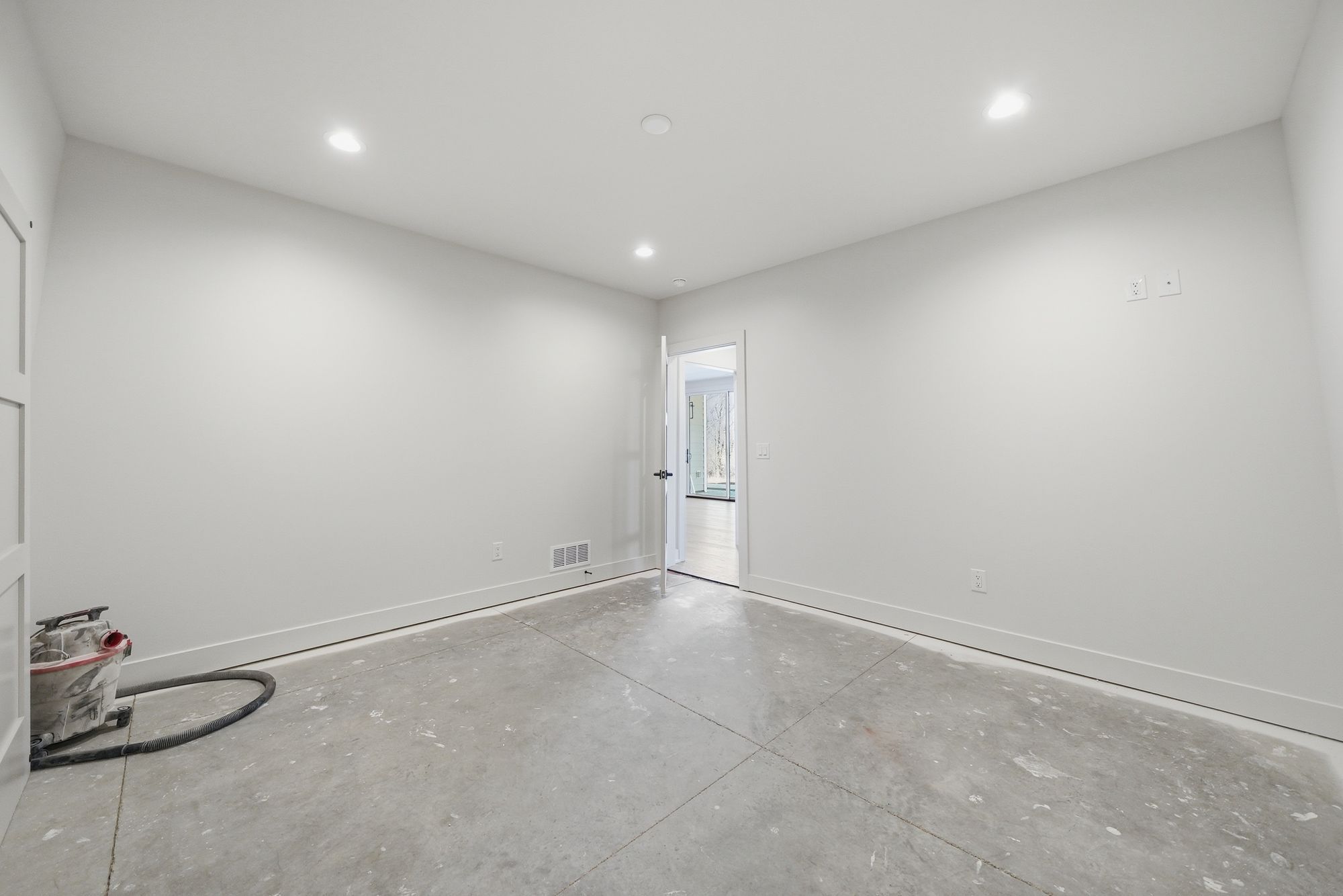 Unfurnished room with light gray concrete floors and white walls with trim and recessed lighting. An open doorway leads to an adjacent space.