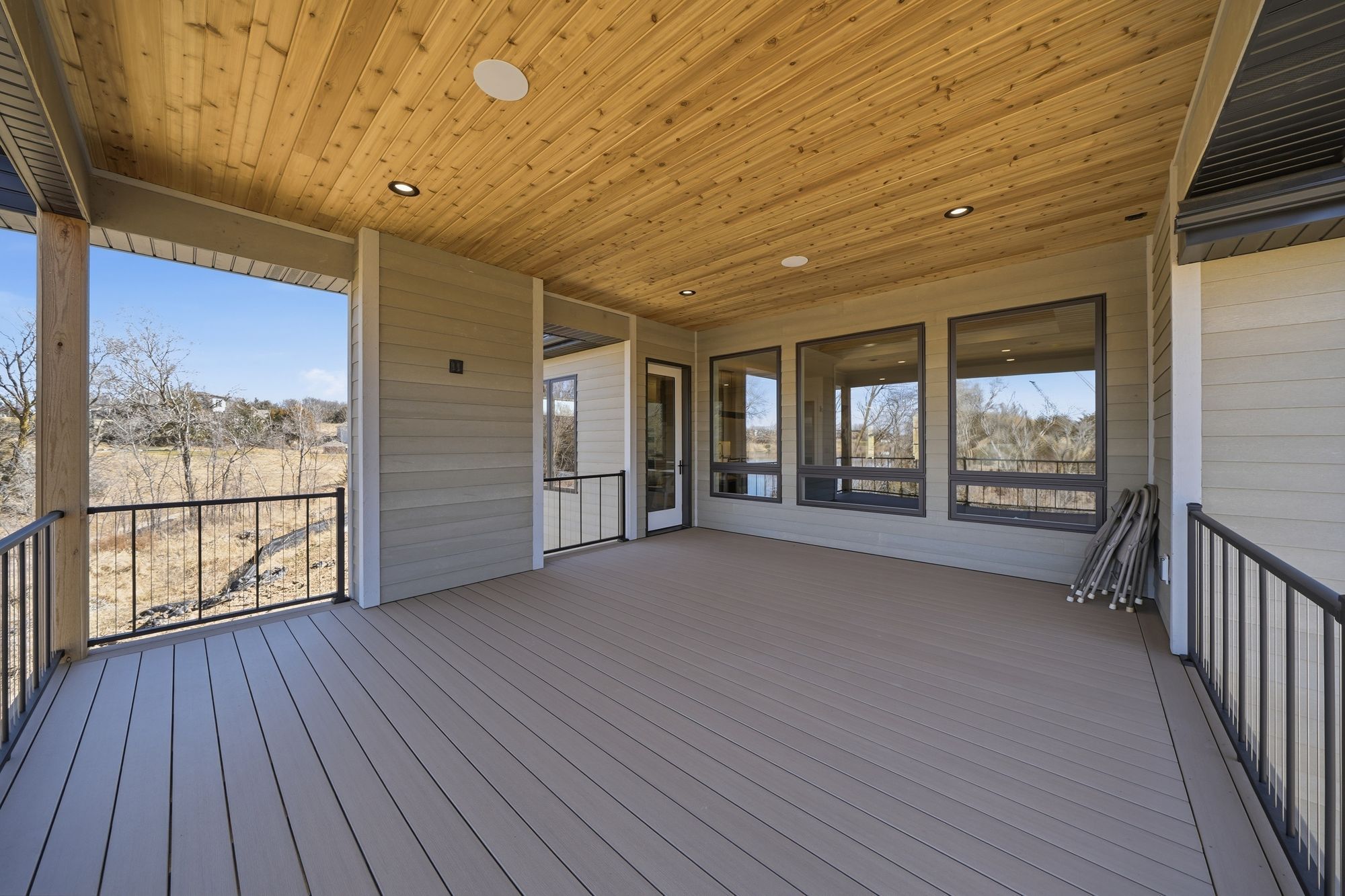 Spacious covered deck featuring wood plank flooring and a tongue-and-groove wood ceiling. The deck is enclosed with black metal railings and overlooks an outdoor landscape.