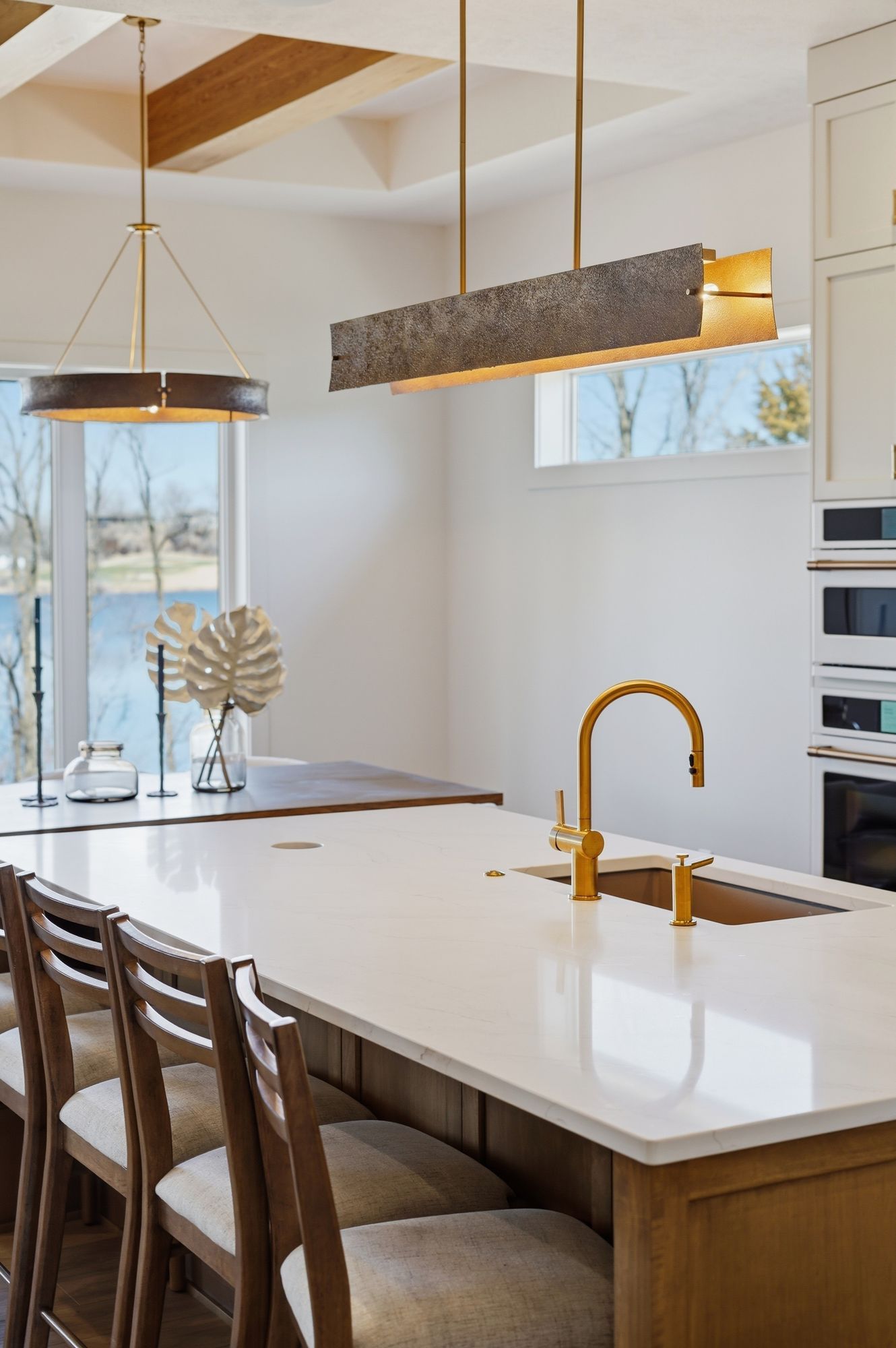 Bright, modern kitchen with a large white marble island and bronze hardware. Open layout with dining space near large windows overlooking the lake.