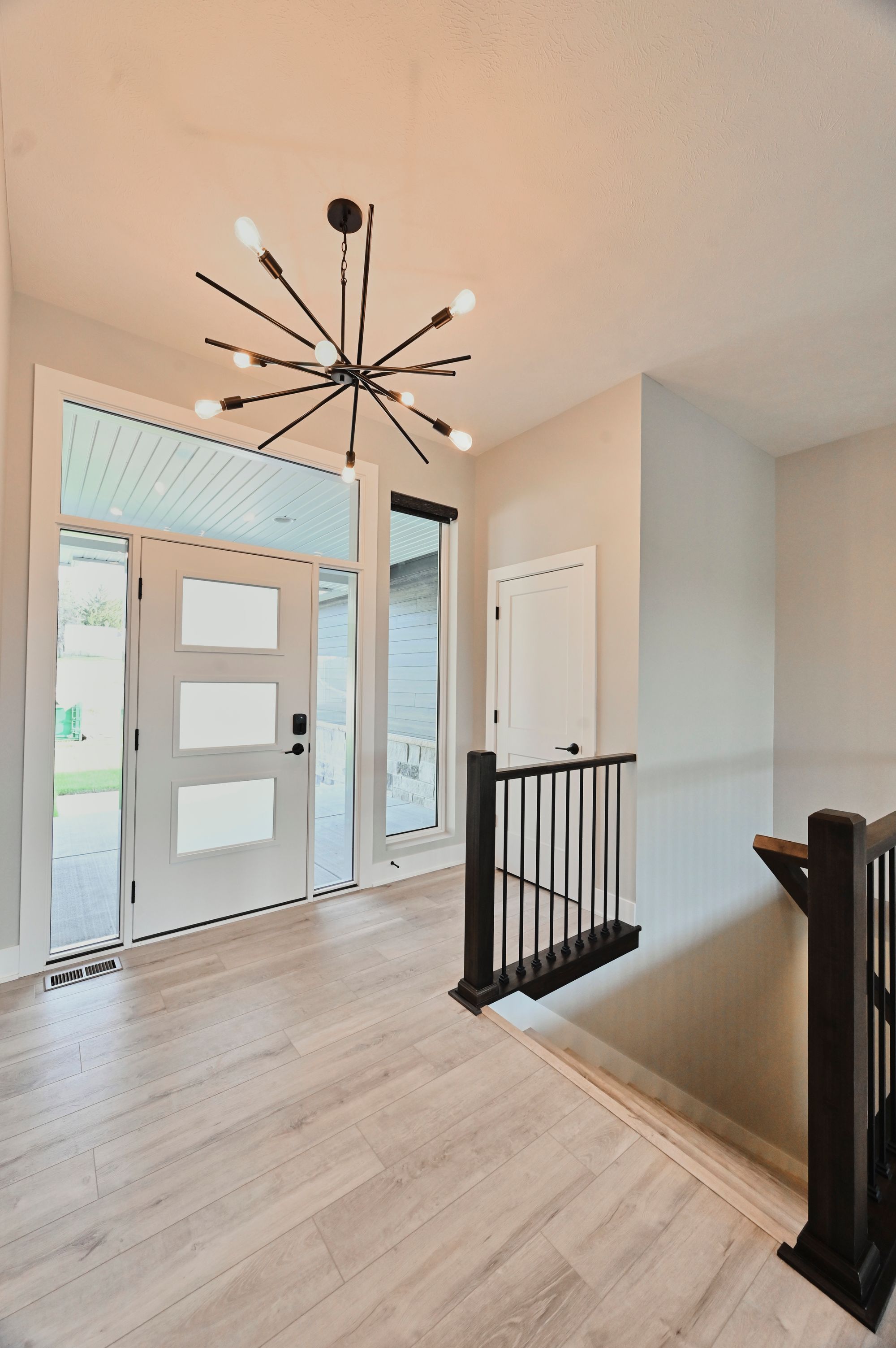 Entryway featuring a modern chandelier, white door with rectangular glass panels, and wood-look tile flooring. Staircase with dark wood railing is also visible.