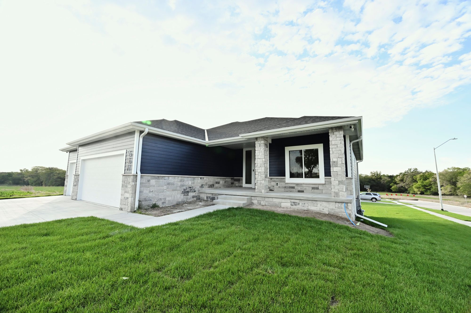 Exterior view of a single-story home showcases navy blue and gray horizontal siding with stone veneer accents, a gabled roof, and a well-maintained lawn. The home features a white garage door and matching trim around the windows and roofline.
