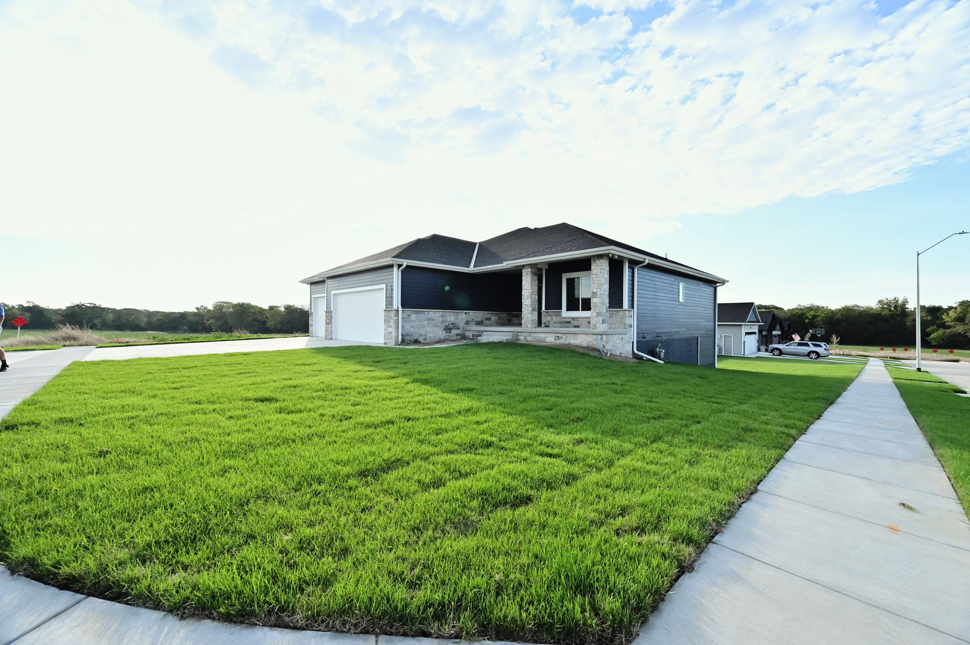 Exterior shot of a single-story home with dark blue siding, stone accents, and a dark roof. The home features an attached garage and a well-maintained green lawn.