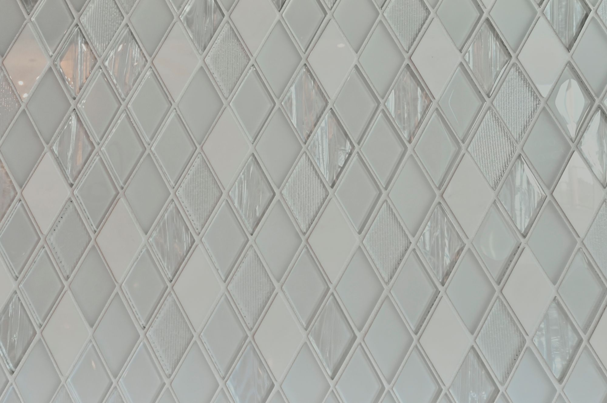 Close-up of a diamond-patterned tile backsplash featuring white and clear glass tiles. The arrangement creates a textured, modern look.