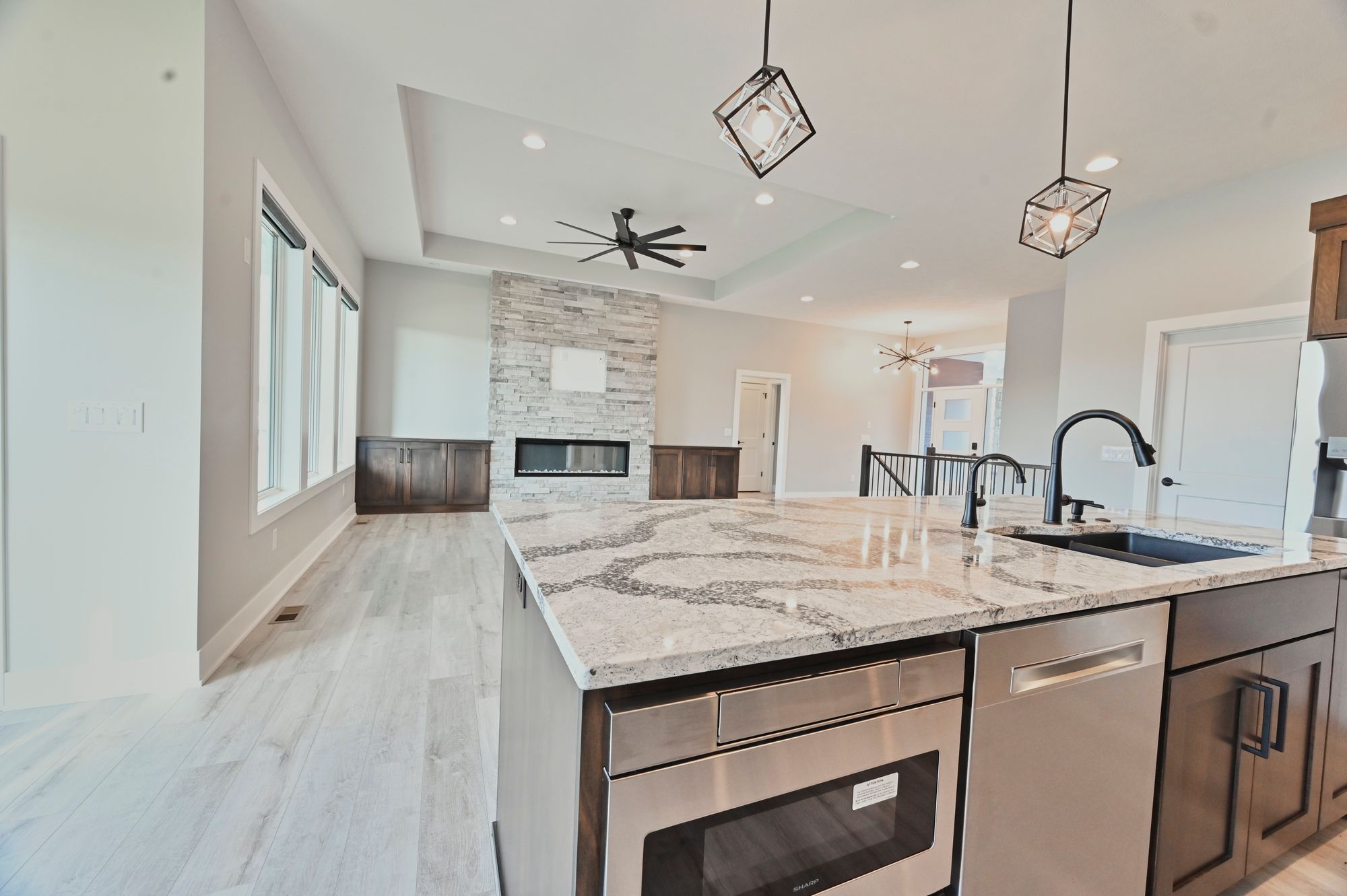 Bright and open kitchen with a large island featuring a granite countertop and stainless steel appliances. The space flows into a living area with a stone fireplace and built-in cabinetry.