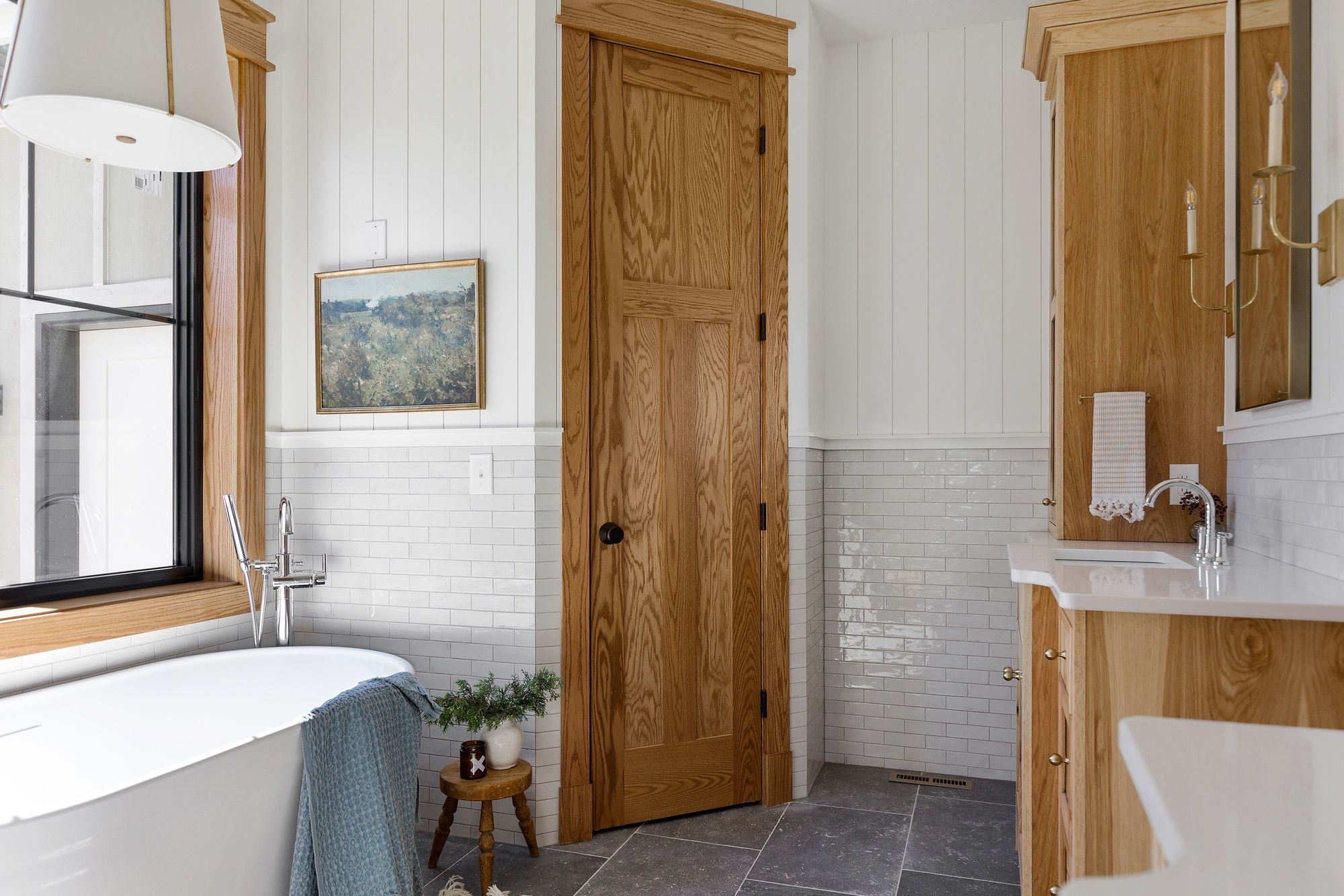 Bathroom showcasing a freestanding tub with chrome fixtures, complemented by a natural wood door and vanity. A potted plant sits on a small stool near the tub, adding a touch of greenery to the space.