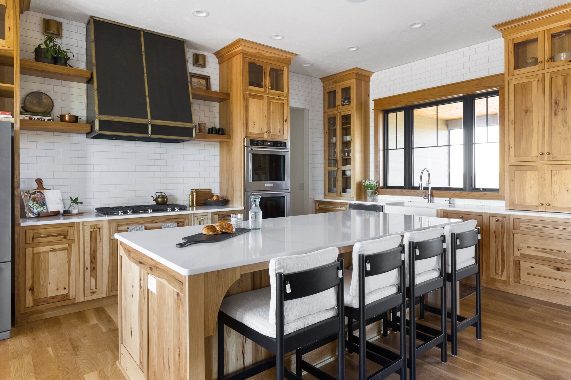 Spacious kitchen with light wood cabinetry, a large white quartz island with seating, and modern appliances. Subway tile backsplash and wood floors complete the space.