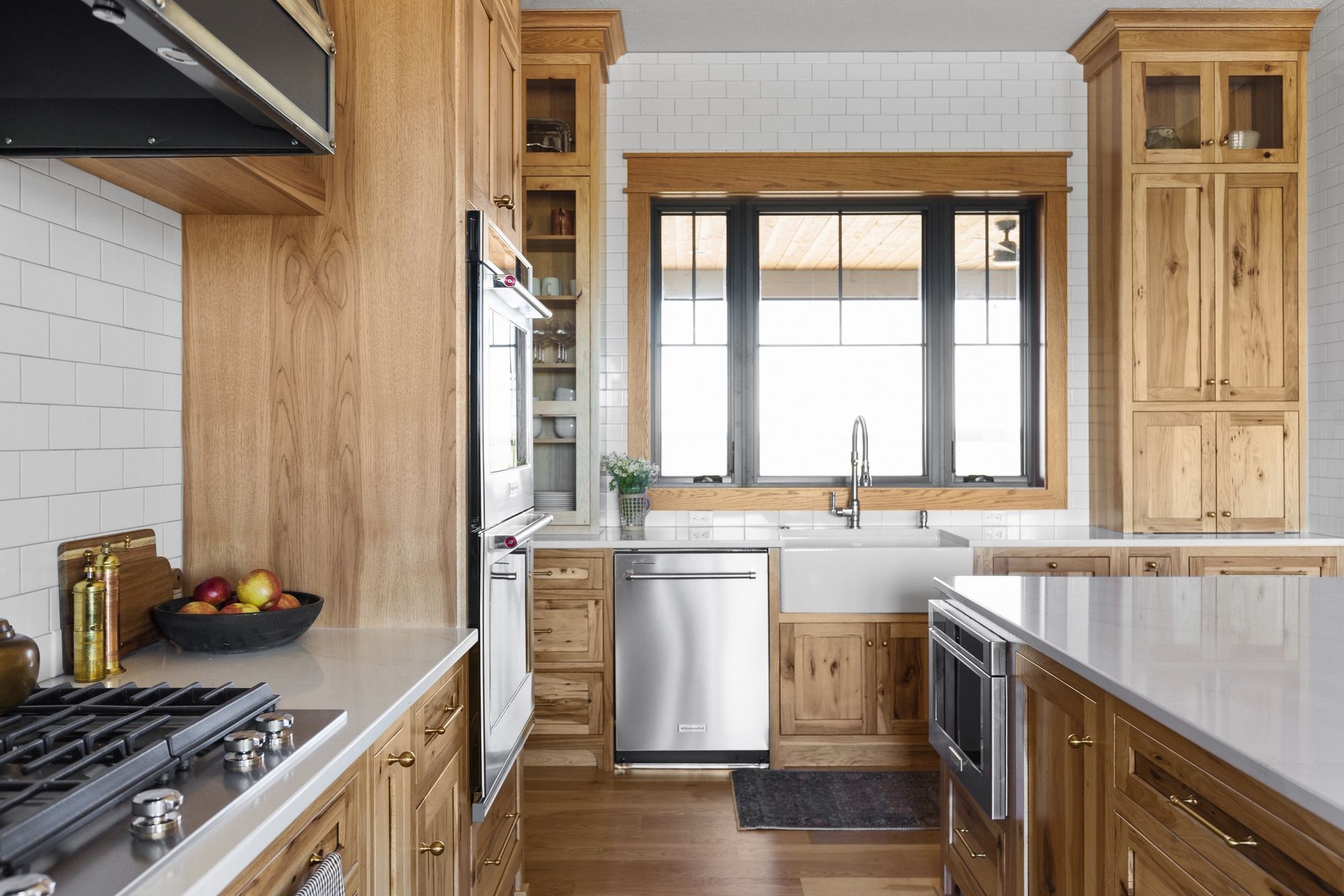 Bright, modern kitchen with light wood cabinetry, white countertops, and stainless steel appliances. The kitchen features a large window above a farmhouse sink, as well as a kitchen island with built-in microwave oven.