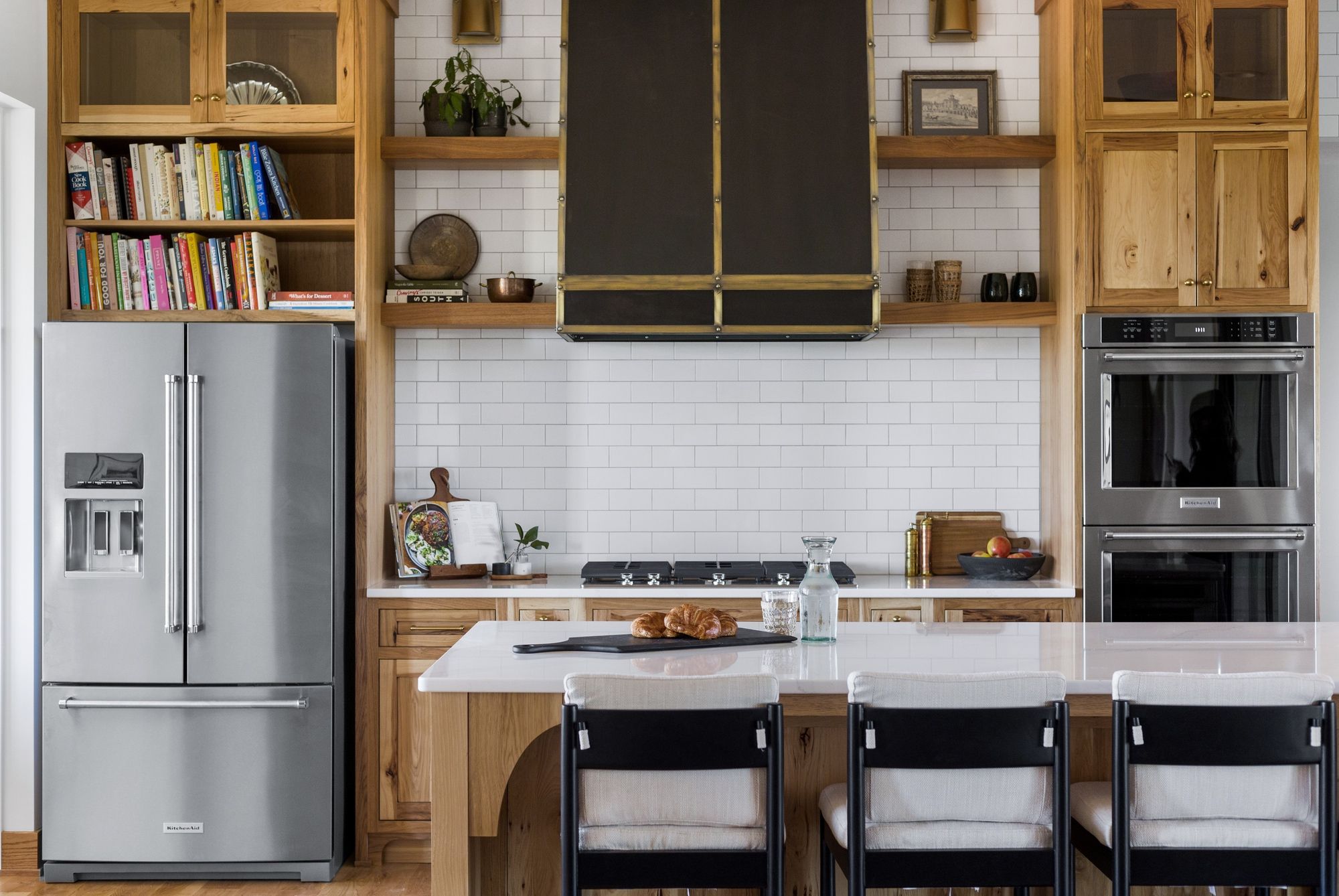 Bright kitchen with custom wood cabinets, stainless steel appliances, and a large island with seating. White subway tile backsplash and dark range hood add modern touches to the traditional space.