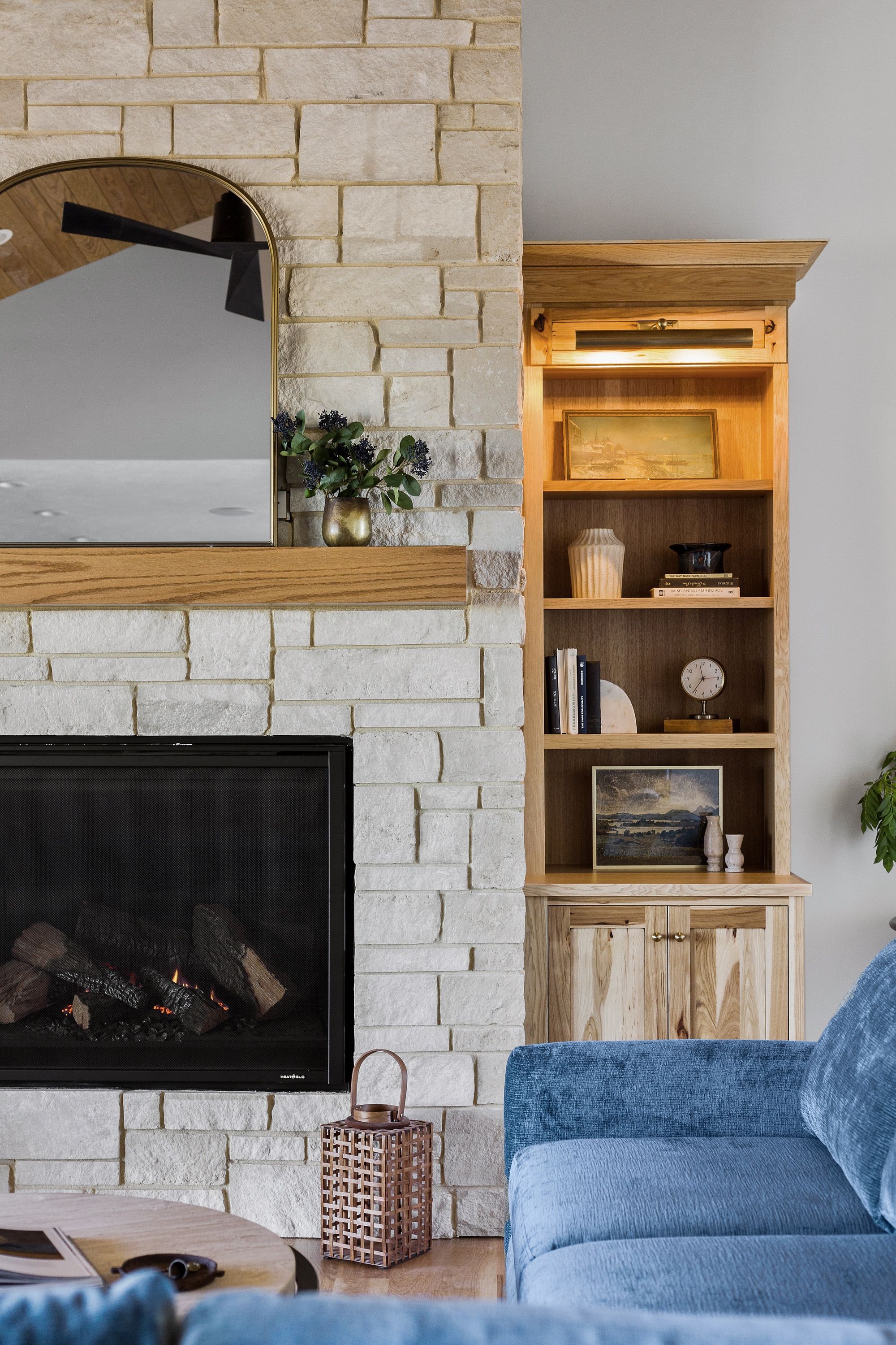 Living room featuring a stone fireplace with wooden mantel and a gold-framed mirror. To the right of the fireplace is a built-in wooden bookshelf displaying books and decorative items.
