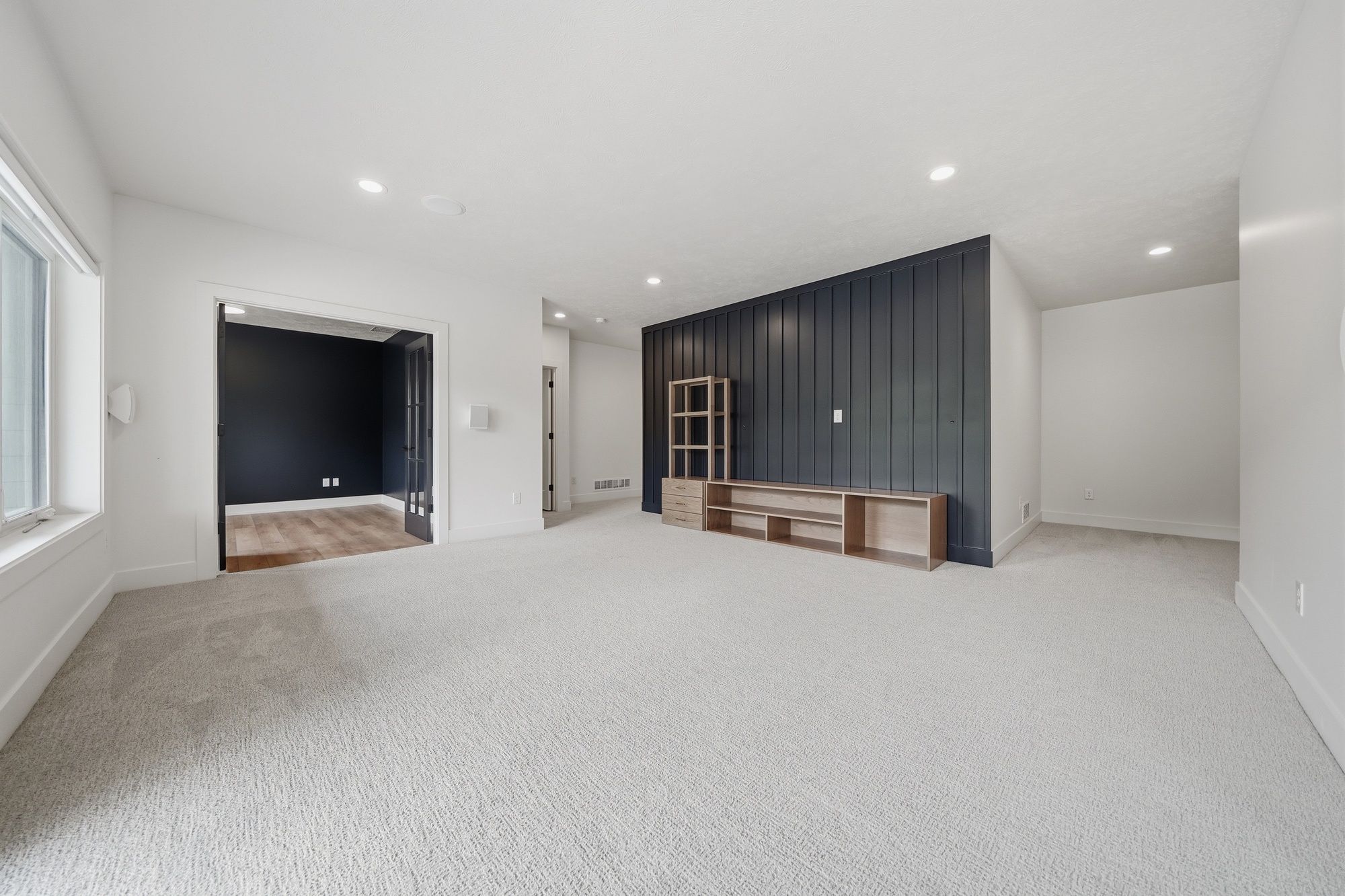 Finished basement family room featuring light gray carpeting, white walls, and a dark blue vertical shiplap accent wall with a light wood entertainment console.