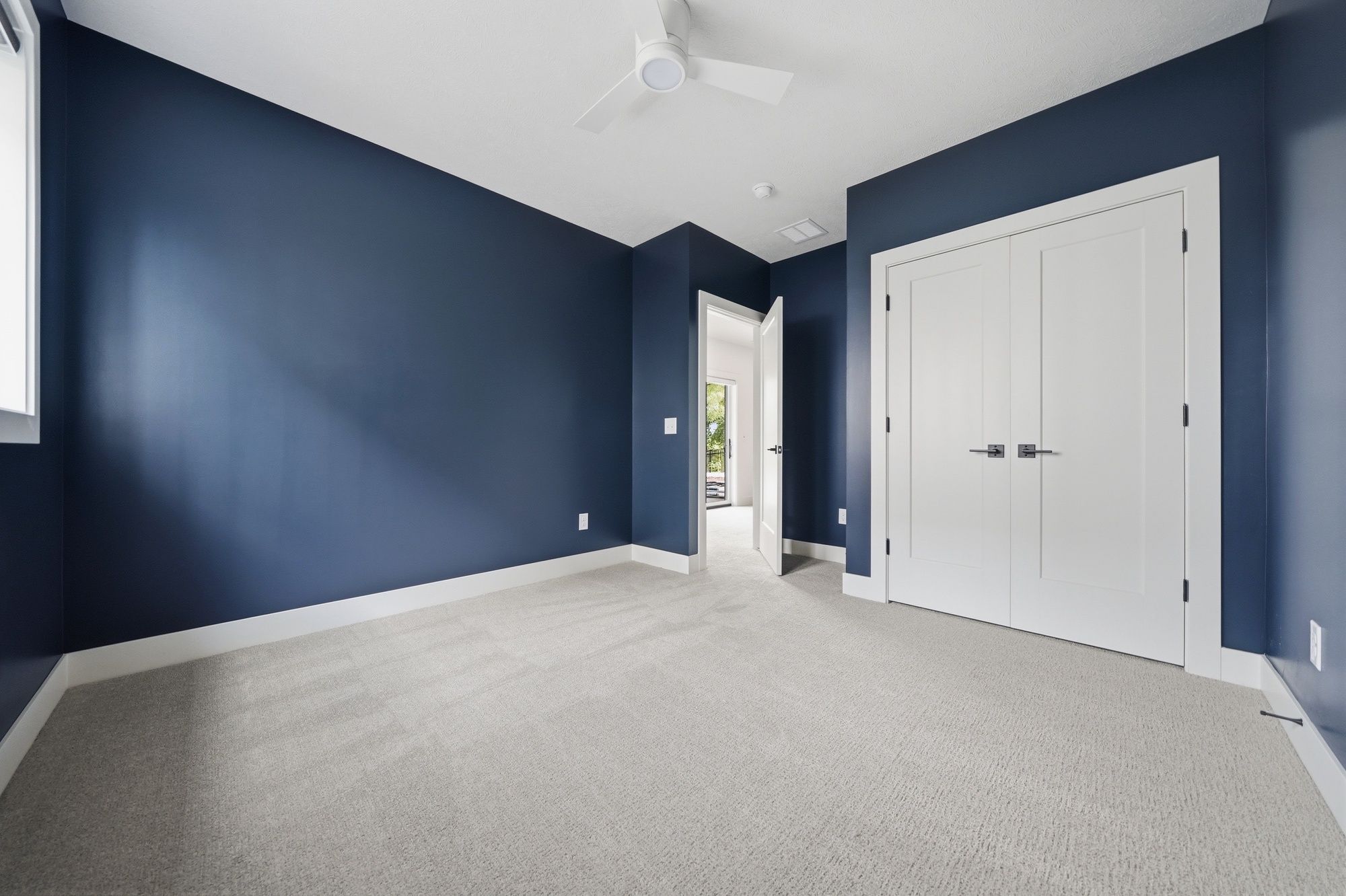 Empty bedroom featuring deep navy blue walls, light gray carpet, white trim, and white double closet doors.