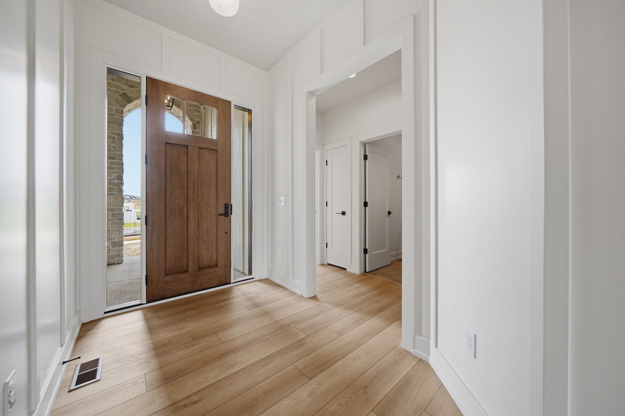 Bright home entryway featuring a rich wood front door with sidelights, board and batten walls, and light oak hardwood floors.