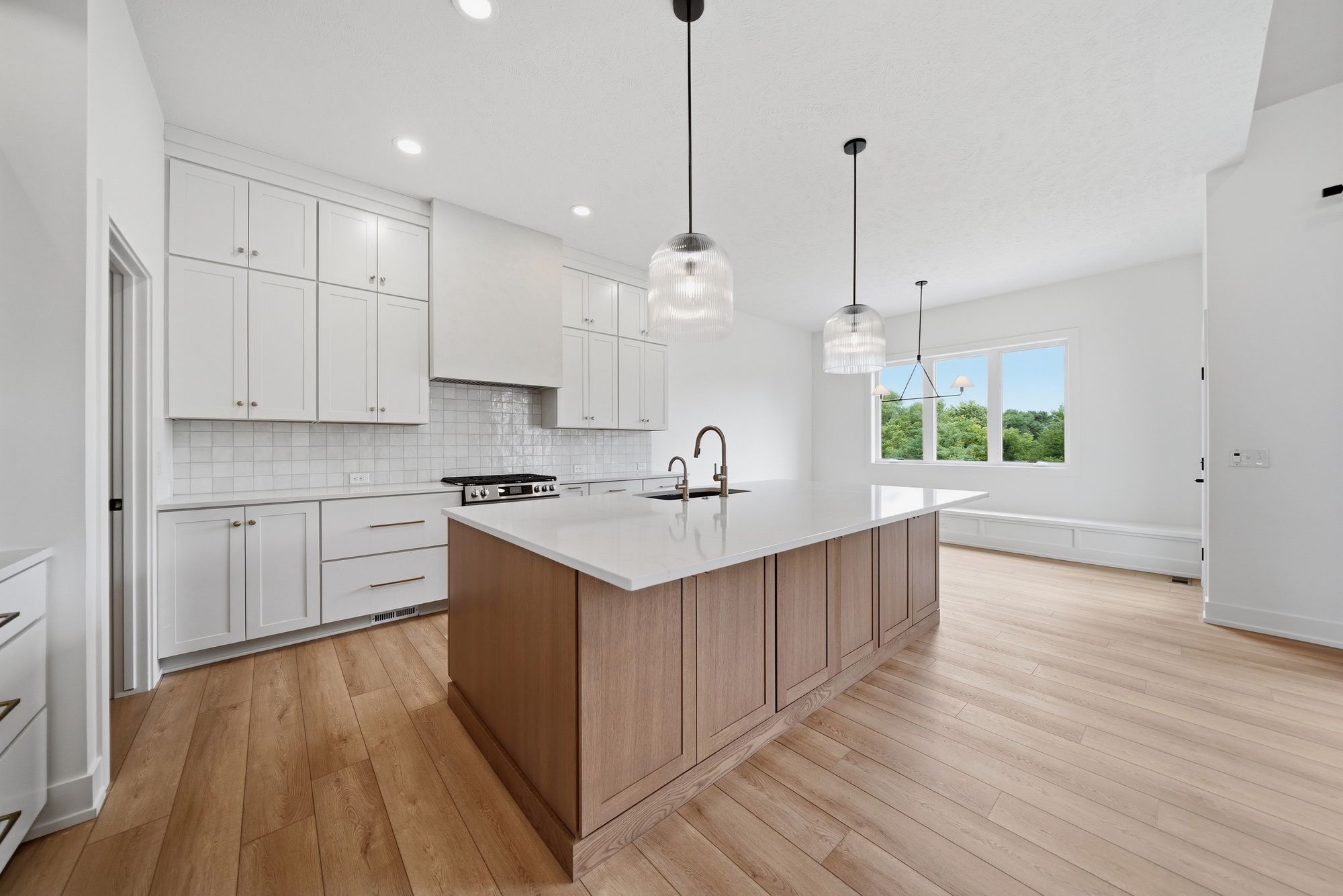 Modern kitchen featuring a light oak island with white quartz countertops, white shaker cabinets, a square tile backsplash, and light hardwood floors.
