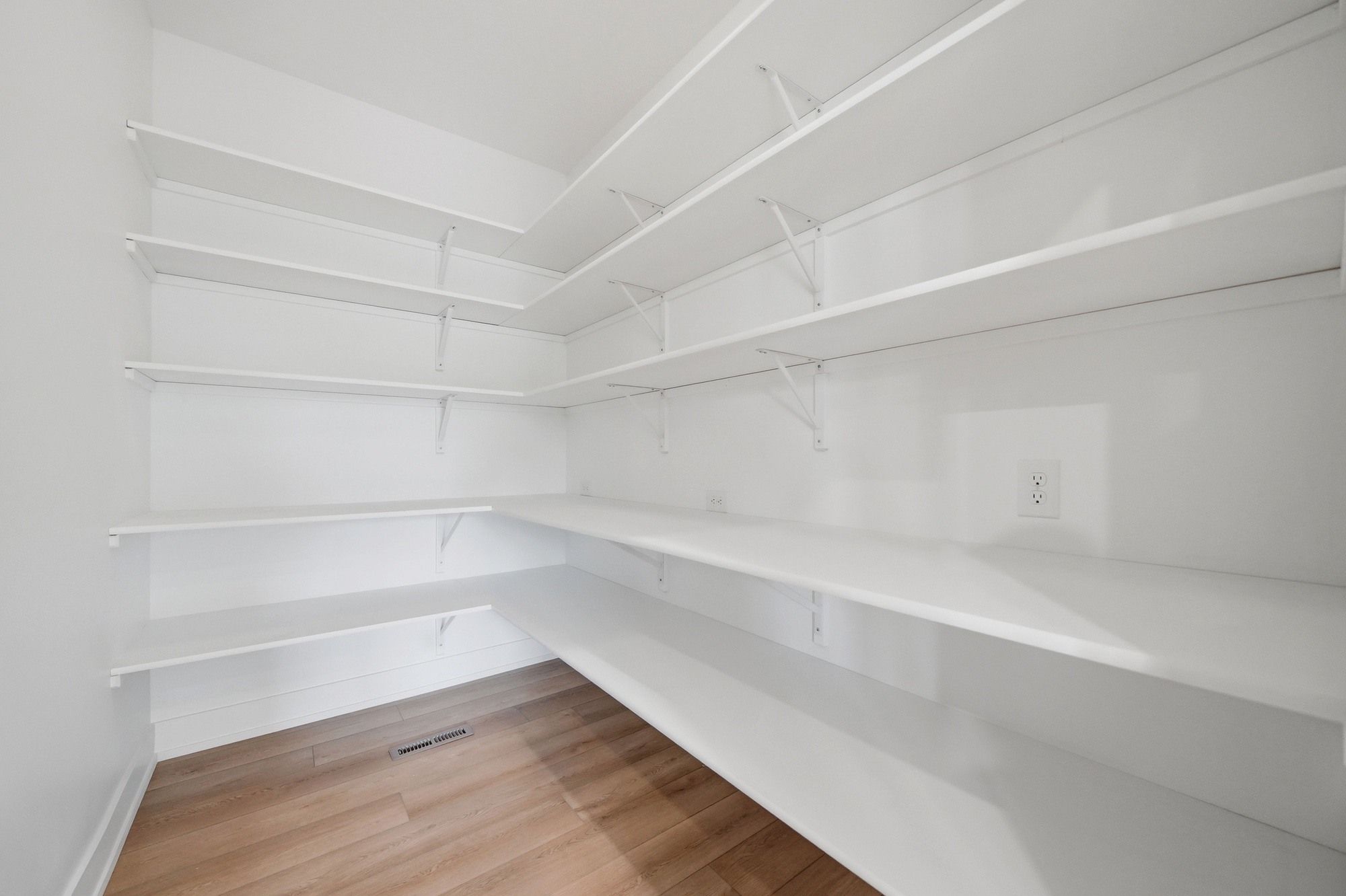 Spacious walk-in pantry with built-in white wrap-around shelves and light hardwood flooring.