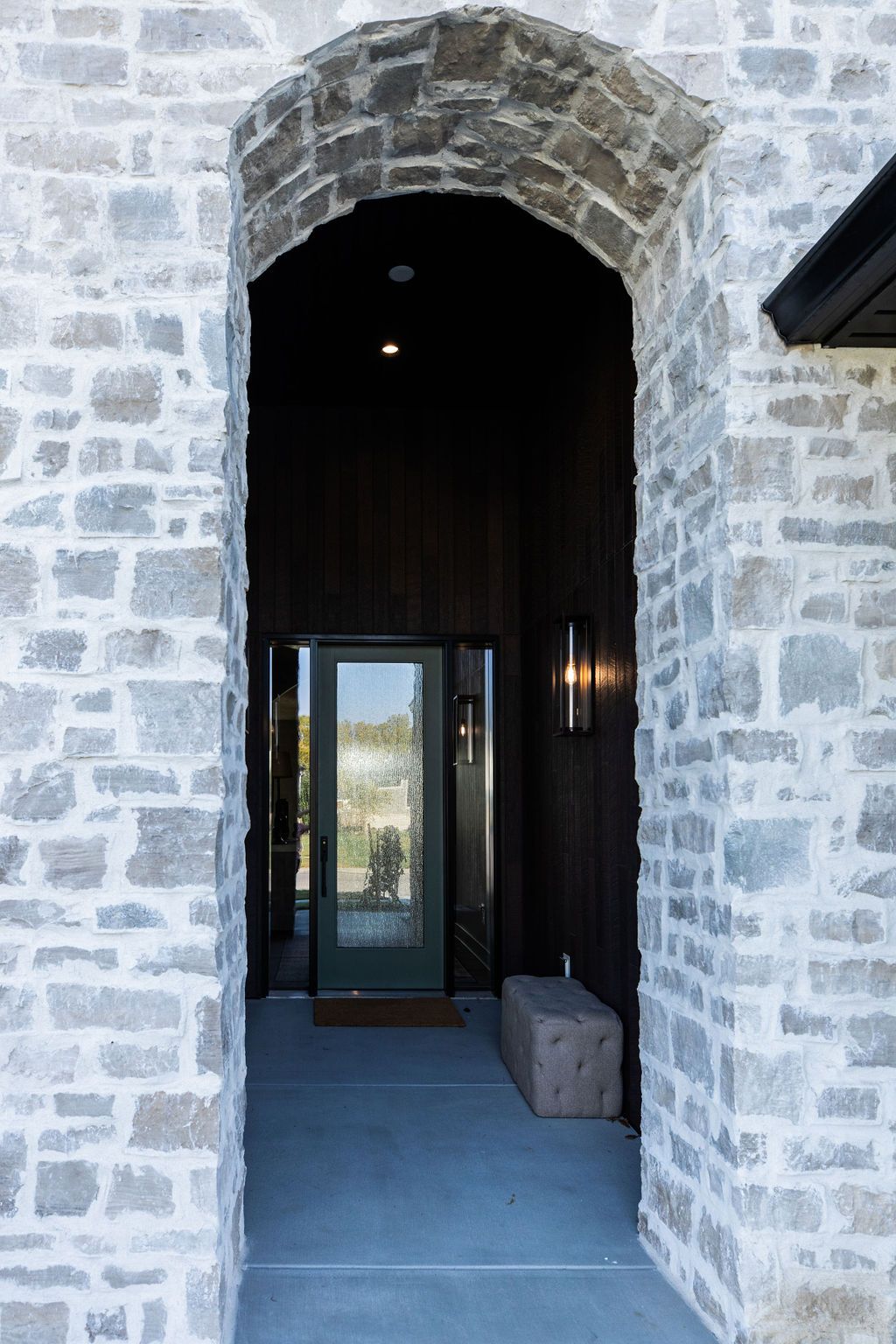 Exterior entryway showcasing a stone archway with a front door. The entrance features dark wood paneling and a stone bench.