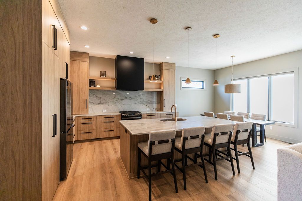 Bright modern kitchen with island seating, wood cabinets, and stainless steel appliances. Dining table and chairs are positioned near a large window with natural light.
